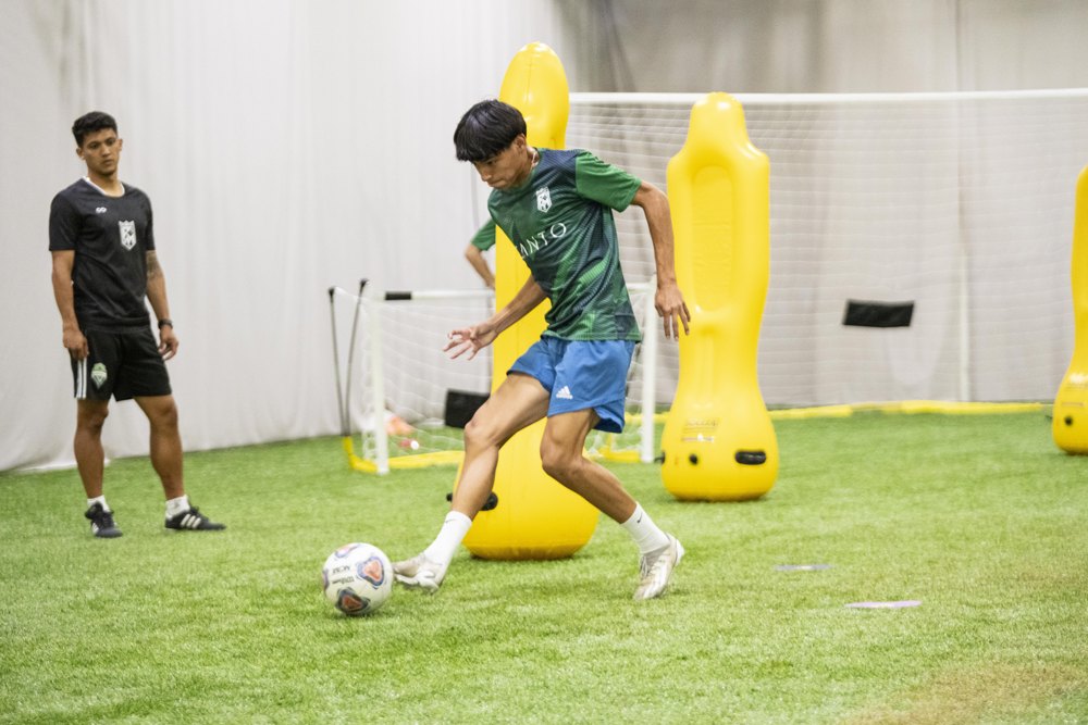 An FM Elite coach watching a player work on technique during indoor soccer training